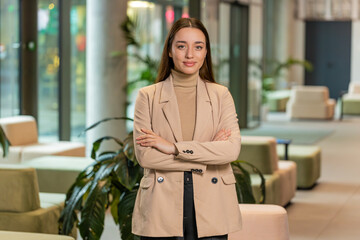 Confident smiling female chief boss in formal clothing looking at the camera. Pretty woman leader office worker looking happy and standing arms crossed in modern office lobby. Businesspeople portraits