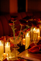 Close-up of a long table with flowers and burning candles in a dark room