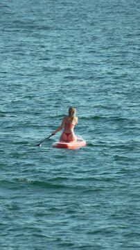 Paddleboarding, woman, ocean, girl in red bikini enjoys summer leisure activity. Vertical video.