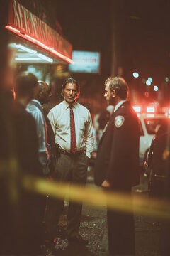 Detective analyzes crime scene with police presence during nighttime investigation