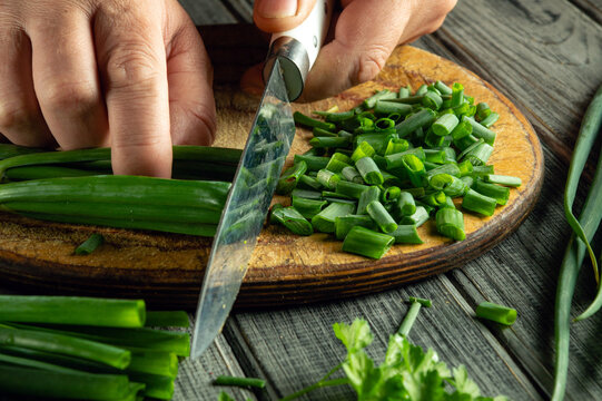Hands skillfully chop bright green onions and fresh herbs on a wooden board. The kitchen atmosphere feels warm and inviting, perfect for cooking - Powered by Adobe