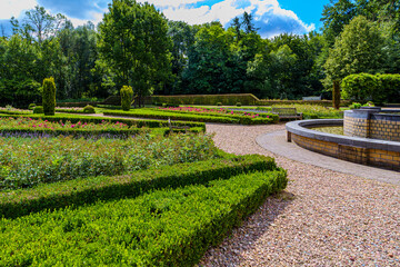 Green bushes, pink flowers, pedestrian paths and fountain, public park in front of TerWorm Castle, surrounded by leafy trees, sunny spring day in Heerlen, South Limburg, the Netherlands