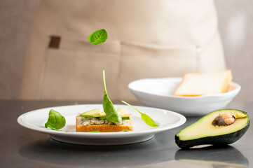 Fresh avocado toast with spinach leaves falling mid-air, captured in a clean kitchen setting. Minimalist food styling emphasizes healthy eating and natural ingredients