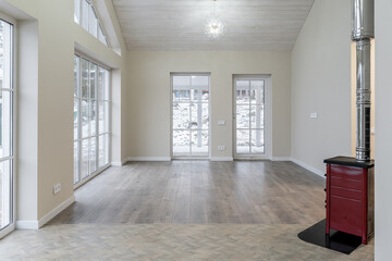 large, empty, bright living room in house. room has many large bright windows, light walls, wooden floor and ceiling, red fireplace, modern chandeliers on ceiling. Architecture inside home