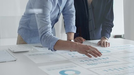 Focused business professionals analyzing financial charts and graphs, discussing market trends and investment strategies while leaning over white desk surface. - Powered by Adobe