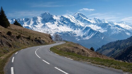 Naklejka premium Scenic mountain road winding up hill towards snow-capped peaks under a blue sky