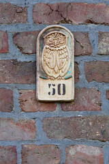 Rustic ceramic plaque featuring a stylized owl perched above the number 50, mounted on an old red brick wall with grey mortar lines, adding a quaint touch.