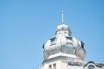 The ornate metal tower of a historic European building with small windows, set against a clear blue...