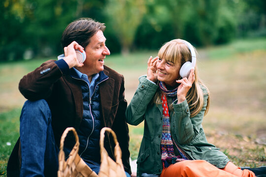 Fototapeta Senior couple sharing music using headphones in park