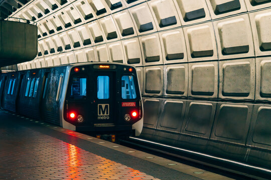 A Washington Metro train enters an underground station with iconic Brutalist architecture.
