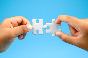 Two hands holding puzzle pieces facing each other on blue background. Concept of teamwork, partnership, connection, collaboration, unity, and problem solving in business or relationship.