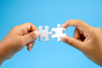 Two hands holding puzzle pieces facing each other on blue background. Concept of teamwork, partnership, connection, collaboration, unity, and problem solving in business or relationship.