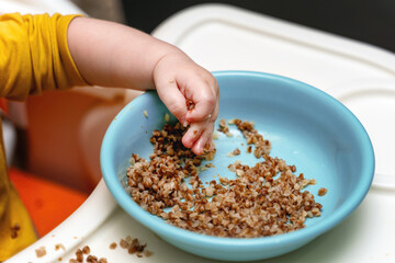 A small child's hand grabbing a fistful of buckwheat porridge during weaning to solid foods