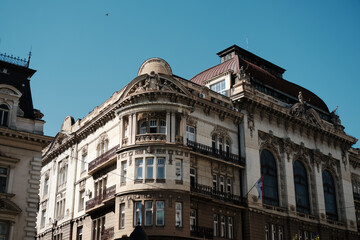 Historic building with ornate balconies and sculptures under a clear blue sky in Belgrade, Serbia. Serbian flag visible on the facade.
