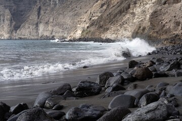 Dramatic Atlantic coast with black volcanic sand, waves splashing on rocks, and cliffs in Tenerife, Canary Islands. Natural coastal landscape with sea foam, volcanic textures, and wild ocean energy.
