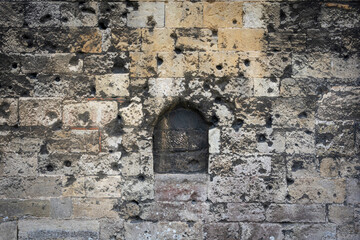 Historic stone wall with a small arched niche and weathered blocks. Rough texture.