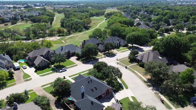 Upscale suburban houses with private pools adjacent to Iron Horse Golf Course in North Richland Hills, Texas. Curving streets, lush trees, and commercial rooftops frame horizon, suburbs Dallas