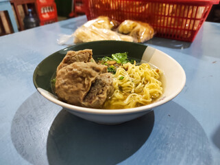 A bowl of chicken noodles with meatball tendons served in a white ceramic bowl. This Indonesian noodle dish is topped with soy sauce-seasoned chicken and meatball tendons and beef.