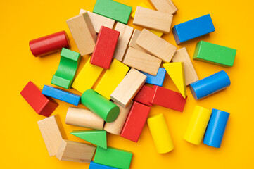 Naklejka premium Wooden children's multi-colored bright construction set blocks of different shapes on yellow background. Montessori style cubes game for toddlers flat lay top view. Concept of learning and education