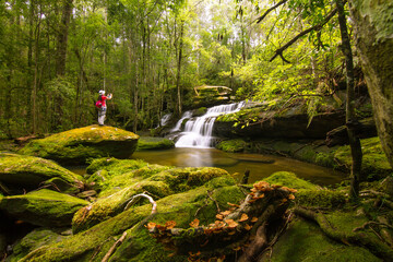 waterfall in the forest with woman taking photo in background 