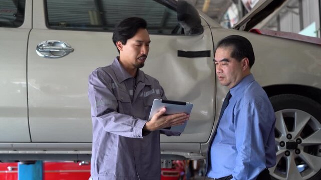Professional Japanese mechanic explains collision damage on a car door and discusses the insurance claim process with a customer trusted consultation, transparency repair service in modern body shop.