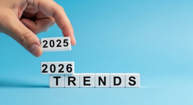 Hand changing 2025 to 2026 on wooden blocks with trend on blue background