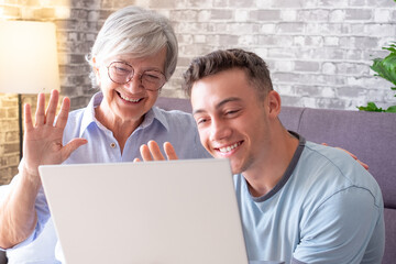 Video call concept. Elderly woman and her young nephew using laptop for online communication via video meeting, smiling caucasian couple waving hand and talking into computer webcam