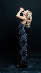 Blonde woman posing confidently in a stylish black strapless paisley dress on a dark background