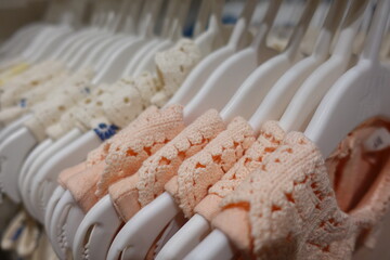 Soft pastel pink blue yellow cream baby clothes neatly arranged on white plastic hangers in a boutique store, highlighting delicate embroidery and gentle cotton texture for newborn girls.