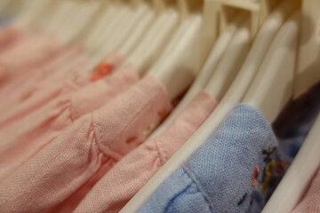 Soft pastel pink blue yellow cream baby clothes neatly arranged on white plastic hangers in a boutique store, highlighting delicate embroidery and gentle cotton texture for newborn girls.