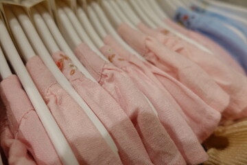 Soft pastel pink blue yellow cream baby clothes neatly arranged on white plastic hangers in a boutique store, highlighting delicate embroidery and gentle cotton texture for newborn girls.