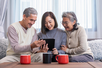 bonding happy asian family,mature adult daughter visit senior parents,sitting on sofa,relaxing,looking on digital tablet together in a cozy room