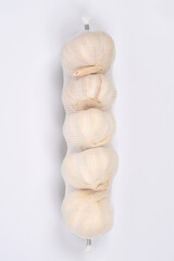 A vertical white mesh bag contains a stack of five garlic bulbs, photographed against a simple white background