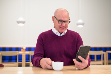 Portrait of senior man using mobile phone while having coffee in cafe
