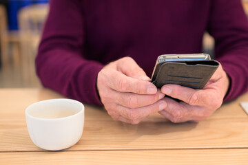 Man using mobile phone at table in cafe. Focus on hands.