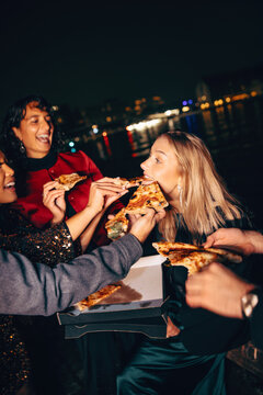 Fototapeta Group of friends sharing pizza by the water during a city night out