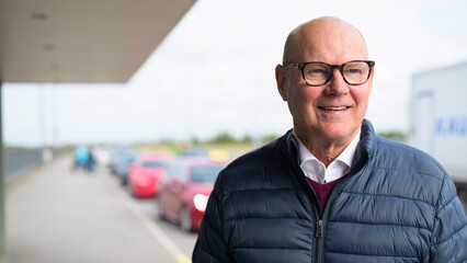 Happy senior Scandinavian man standing outdoors in front of a car park at an airport taxi area © Ranta Images
