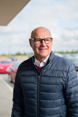 Happy senior Scandinavian man standing outdoors in front of a car park at an airport taxi area