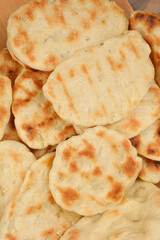 A close-up shot of a pile of small, round flatbreads with golden-brown grill marks, suggesting they were cooked on a skillet