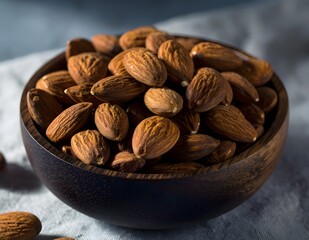 Close-up of roasted almonds in a dark wooden bowl on a textured surface, captured with natural light and shallow depth of field. Perfect for healthy food, snack, and organic nutrition concepts.
