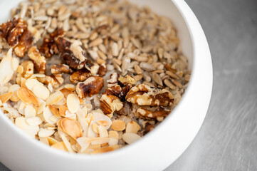 Close-up of raw mixed nuts and seeds in a white bowl, including sunflower seeds, almonds, and walnuts. Healthy snack or breakfast ingredient. Natural, rustic, top view.
