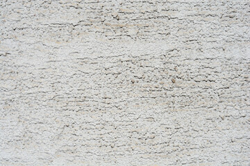 A close-up, horizontal shot of a rough exterior wall texture covered in a fine, light gray pebbled stucco finish with horizontal grooves