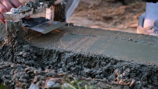 A construction worker smooths wet concrete with trowel in formwork on a building site. Smoothing to create a flat surface. Professional hand work with foundation. High quality 4K footage.