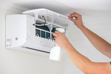 Hands Cleaning the Air Conditioner Unit Filter with a Disinfectant Spray Bottle