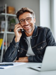 Confident digital nomad man smiling during business call, working from bright minimalist office desk with laptop, casual professional look.