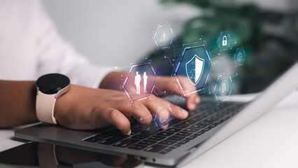 Hands typing on a laptop keyboard with a digital overlay of cybersecurity icons, including a shield, fingerprint recognition, and a padlock. Represents advanced data protection, system security.