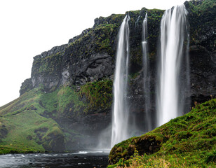 A stunning waterfall cascades down a rocky cliff, surrounded by lush green vegetation and flowing water in a serene natural landscape.