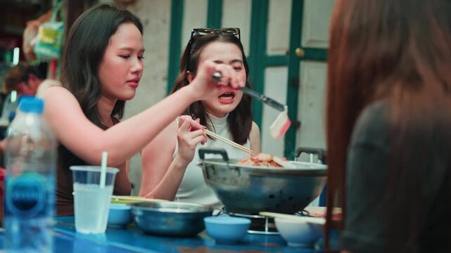 Group of asian friends sharing and eating hotpot at a street food table, smiling and enjoying delicious meal in a casual outdoor setting showing culture, friendship and lifestyle