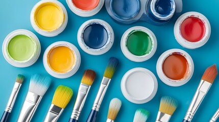 Overhead view vibrant watercolor paints with various paintbrushes on blue paper