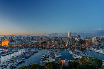 Sunlit Marina with Yachts and Modern City Skyline under Blue Sky